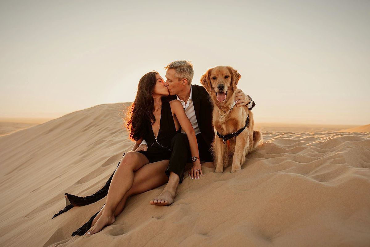 Pareja feliz con un receptor dorado besándose en una duna de arena